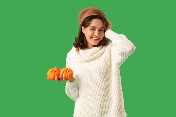 Young woman with pumpkins on green background