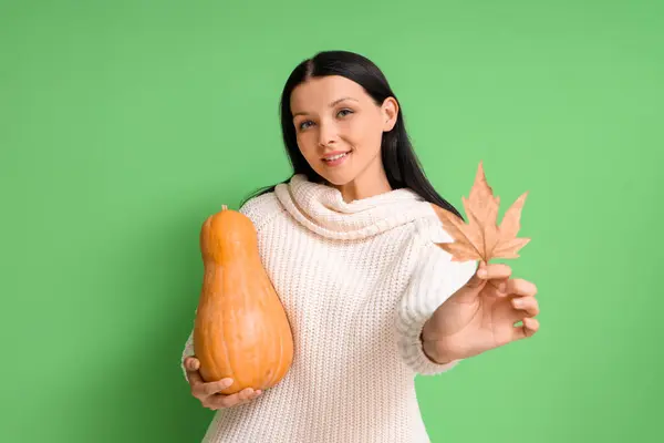 Beautiful woman with pumpkin and autumn leaf on green background