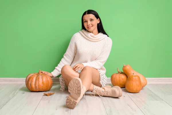 Beautiful woman with pumpkins sitting near green wall