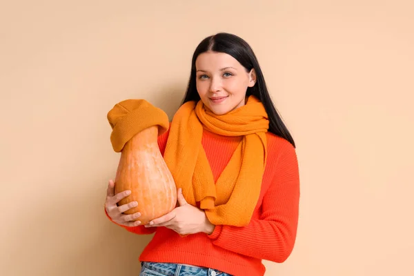 Beautiful woman with pumpkin in hat on beige background