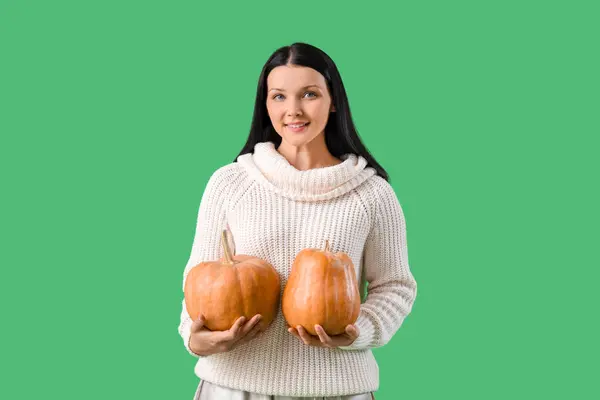 Beautiful woman with pumpkins on green background