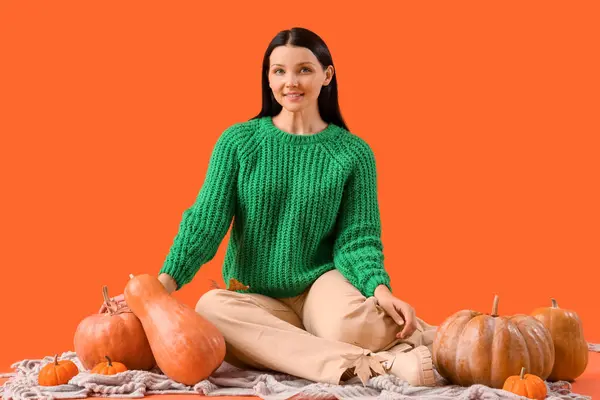 Beautiful woman with pumpkins sitting on plaid against orange background