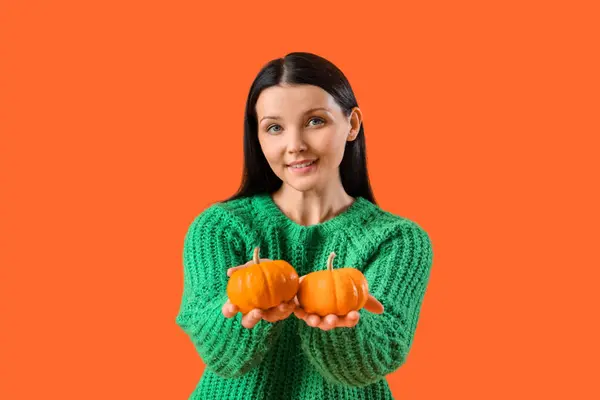 Beautiful woman with pumpkins on orange background