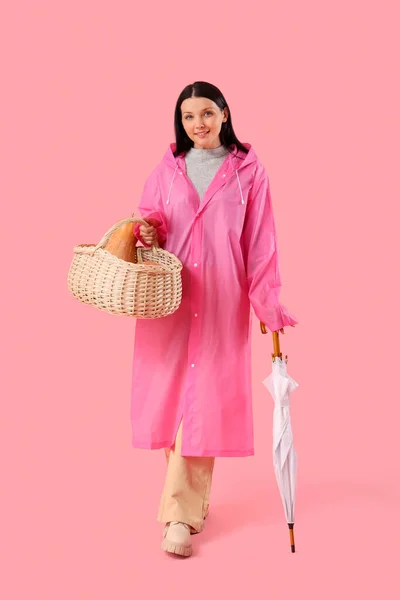 Beautiful woman with pumpkins in basket and umbrella on pink background
