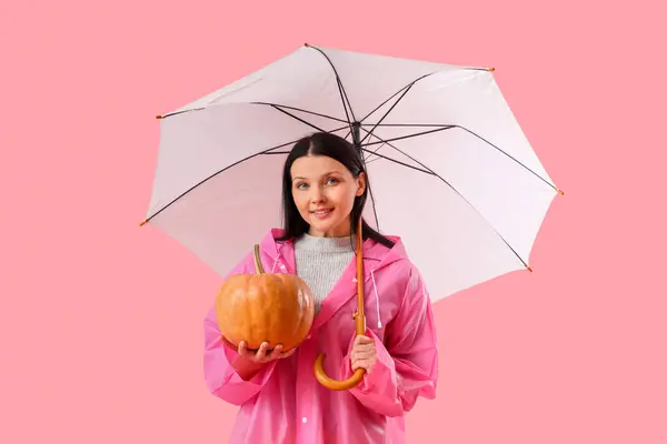 Beautiful woman with pumpkin and umbrella on pink background