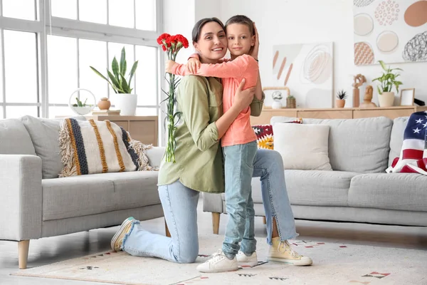 stock image Little boy with carnation flowers hugging his mother at home. Veterans Day celebration