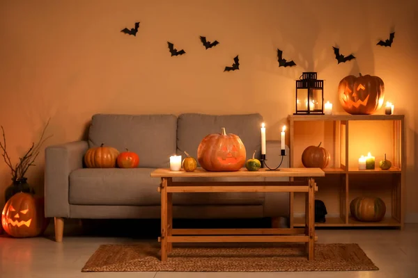 Interior of dark living room with Halloween pumpkins and burning candles
