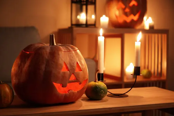 Halloween pumpkins with burning candles on table in dark living room, closeup