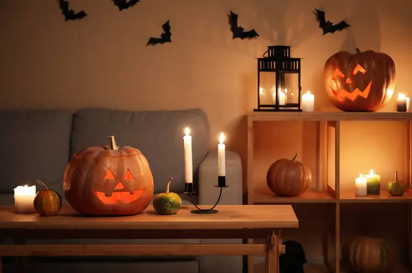 Halloween pumpkins with burning candles on table in dark living room