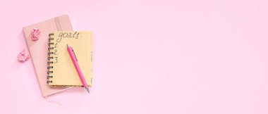 Liste yapmak için boş defterler ve yazı için yeri olan pembe arkaplan üzerine kalem. Yeni yıl hedefleri