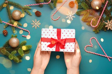 Hediye kutusu ve mavi arka planda Noel dekoru olan kadın elleri.