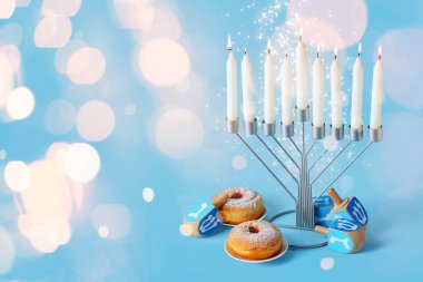 Hannukah kutlamaları için parlak mumlar, eşyalar ve çörekler açık mavi arka planda ve metin için yer var