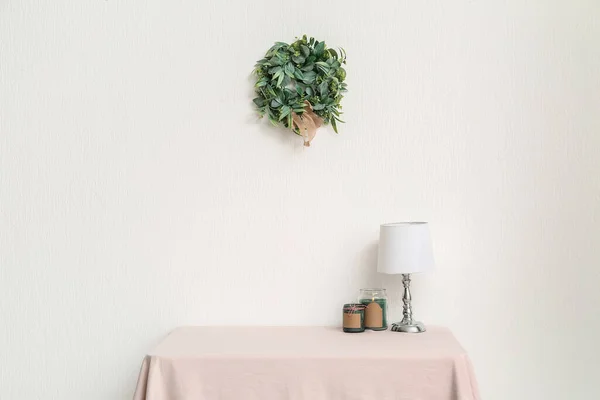 Dining table with candles, lamp and Christmas mistletoe wreath on light wall