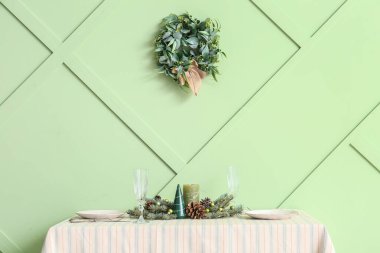 Sofralı yemek masası ve yeşil duvarda Noel ökseotu çelengi.