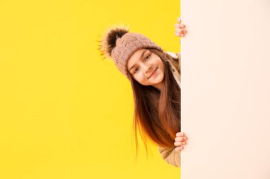 Sarı arka planda boş posteri olan kışlık elbiseli şirin küçük kız.