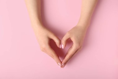 Kadın pembe arka planda elleriyle kalp yapma
