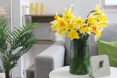 İçinde çiçek açan vazo ve oturma odasının içindeki sehpanın üzerindeki saat.