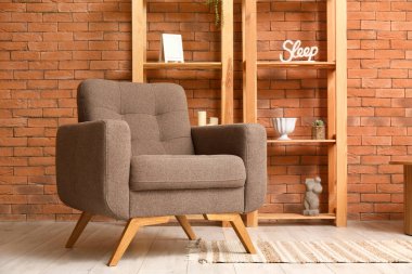 Kahverengi tuğla duvarın yanında rahat koltuk ve raf ünitesi