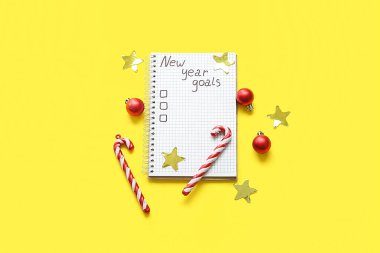 Listesi boş bir defter, baston şekerler ve sarı arka planda Noel topları. Yeni yıl hedefleri