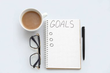 Listesi boş bir defter, beyaz arka planda bir fincan kahve ve gözlük. Yeni yıl hedefleri