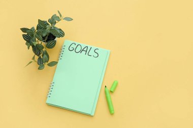Yapılacaklar listesi boş bir defter, sarı arka planda işaretleyici ve bitkiler. Yeni yıl hedefleri
