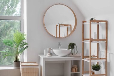 Lavabosu, banyo aksesuarları, aynası ve raf ünitesi olan hafif bir banyo.