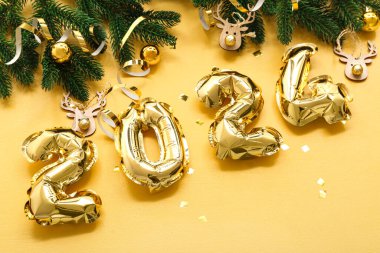 2024 numaralı şekil folyo balonlardan, köknar dallarından ve sarı arka planda Noel süslemelerinden oluşmuştur.