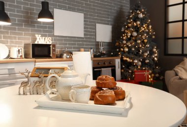 Modern mutfaktaki masada tarçınlı çörekler, fincanlar, çaydanlık ve Noel dekoru.