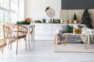 Açık uzay mutfağının içi gri kanepe, beyaz masa ve Noel dekoruyla dolu.