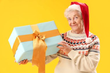 Sarı arka planda Noel Baba şapkalı son sınıf kadını.