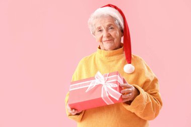 Noel Baba şapkalı yaşlı kadın pembe arka planda Noel hediyesi ile