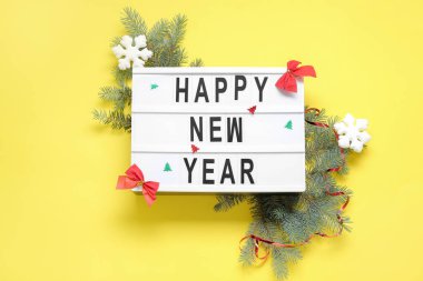 Yeni yılın kutlu olsun yazılı tahtası ve sarı arka planda Noel süslemeleri