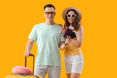 Sarı arka planda pasaportları ve bavulları olan genç bir çift.