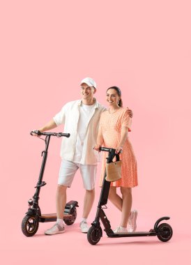 Pembe arka planda elektrikli bisikleti olan hamile bir çift.