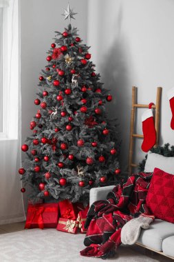 İçinde Noel ağacı, hediye kutuları, çoraplar ve gri kanepe olan oturma odası.