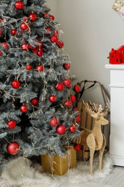Kırmızı topları olan Noel ağacı, hediye kutusu, tahta geyik ve oturma odasında kızak.