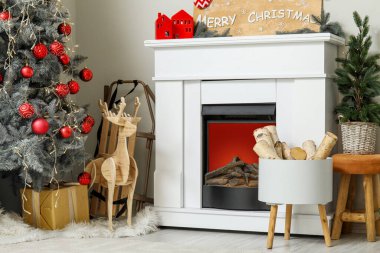 Kırmızı topları olan Noel ağacı, hediye kutusu, tahta geyik ve şömine oturma odasında.