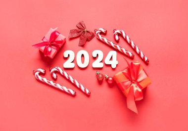 Noel topları, hediye kutuları ve kırmızı arka planda şeker kamışlarıyla 2024 'ü düşün.
