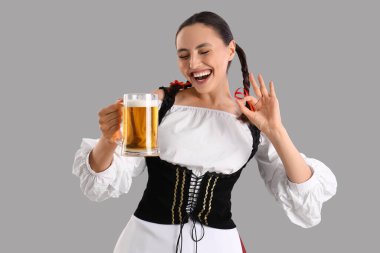 Geleneksel Alman elbiseli genç bir kadın ve bira gri arka planda iyi görünüyor.
