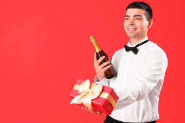 Kırmızı arka planda şampanya ve Noel hediyesi olan genç bir adam.