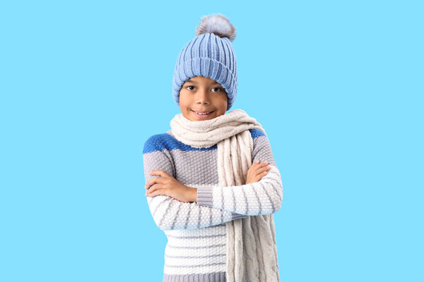 Cute African-American boy in warm winter clothes on blue background