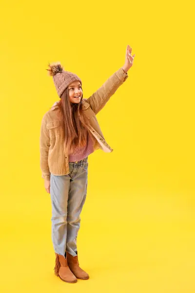 Cute Little Girl Zimie Ubrania Machając Ręką Żółtym Tle — Zdjęcie stockowe
