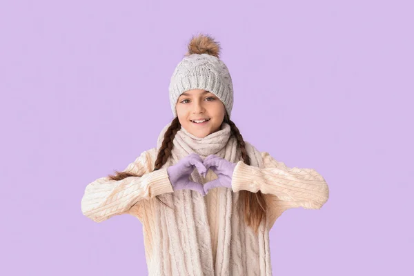 冬の服でかわいい少女ライラックの背景に手でハートの形を作る — ストック写真