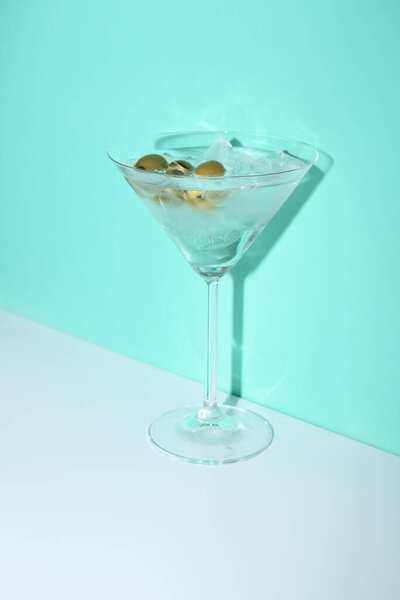 Glass of martini with olives and ice on color background