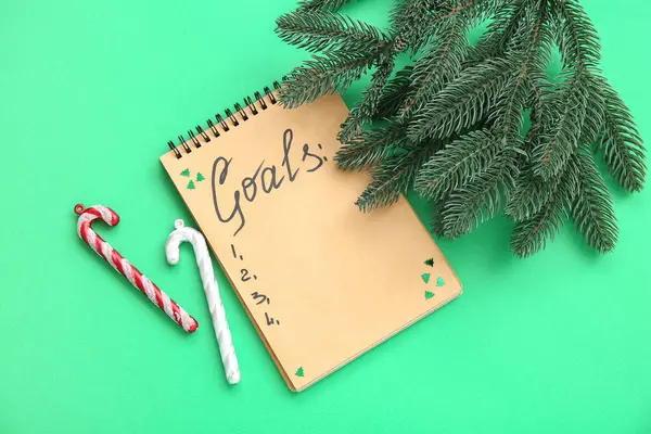 Notebook with empty to do list, candy canes and fir branches on green background. New year goals