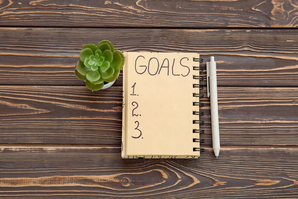 Notebook with empty to do list, houseplant and pen on brown wooden background. New year goals