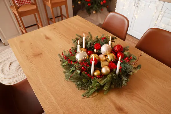 Christmas composition with wreath, burning candles, red berries and balls on table in kitchen