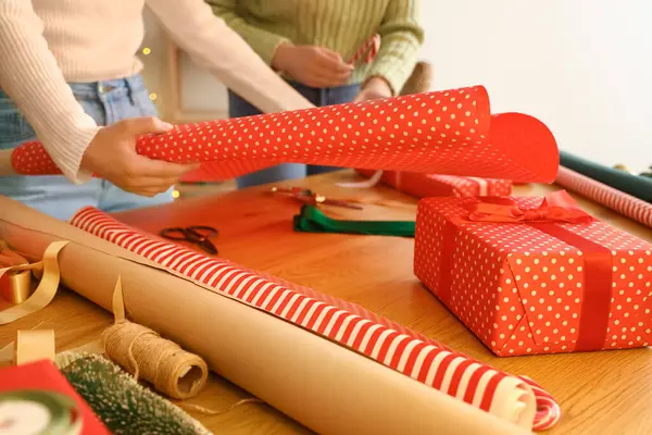 Young women with wrapping paper for Christmas gift at table, closeup