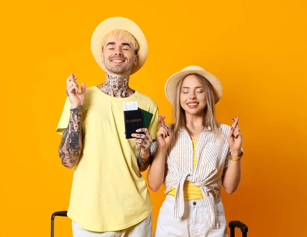 Young couple with passports crossing fingers on yellow background