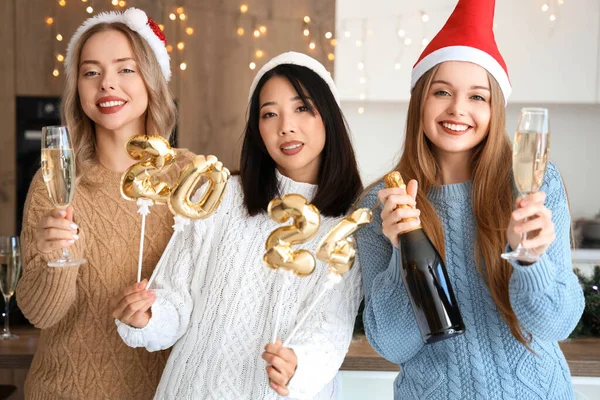 Young women with champagne and figure 2024 celebrating Christmas in kitchen